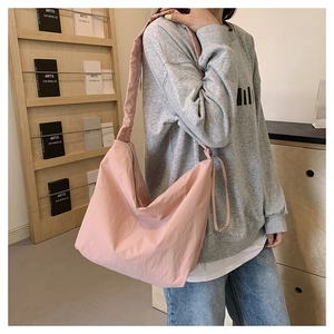 Pink nylon crescent shoulder bag shown on model in a cozy minimalist home setting