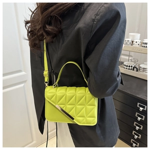 Detail of lime green quilted handbag with gold metal bar worn with a black suit