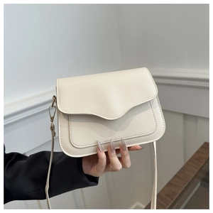 Close-up of cream PU leather crossbody bag with wavy flap and bronze metal clasp detail