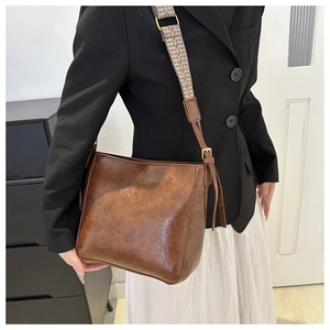 Détail du sac seau marron en cuir texturé avec une bandoulière tissée en jacquard