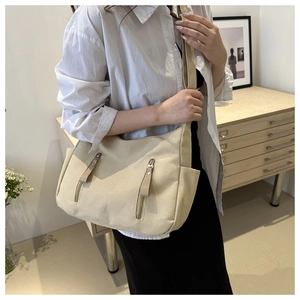 Detailed shot of beige canvas tote bag featuring double metal zipper pockets and side slots