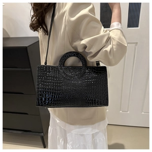 Detail of black crocodile texture patent leather bag with circular cutout handle and strap