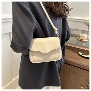 Close-up of off-white crossbody bag with wave-edged flap and adjustable gold buckle strap