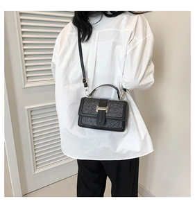 Detail view of black glitter crossbody bag featuring gold H-shaped clasp and leather strap