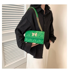 Detail of green quilted bag with golden bow clasp and leather chain strap on model