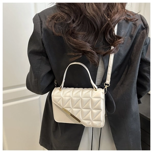 Detail of white quilted crossbody bag with gold metal trim worn over a black blazer