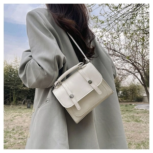Detail of a minimalist cream rectangular crossbody bag with circular metal buckle accent