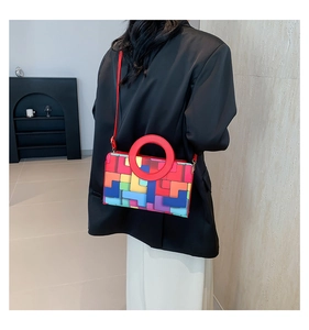 Detail of colorful geometric block pattern and red round handle on textured handbag