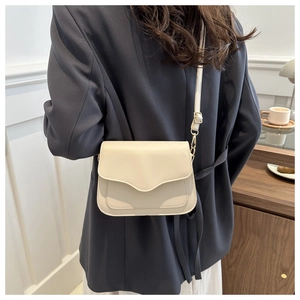 Detail view of the beige crossbody bag showing curved flap design and gold buckle adjustment