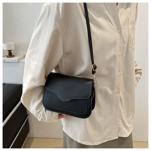 Detail showing black leather crossbody bag with curved flap and gold hardware on model