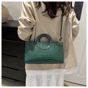 Detail of dark green crocodile pattern shoulder bag with circular cutout handle and strap