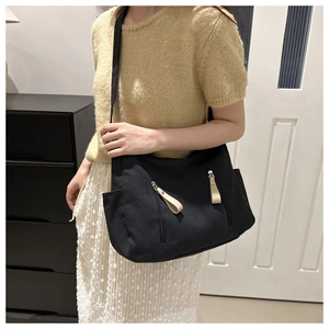 Side view of a large black canvas dumpling bag with leather zipper tabs and side pockets