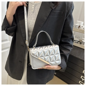 Detail view of silver quilted crossbody bag with gold hardware on a model in black suit
