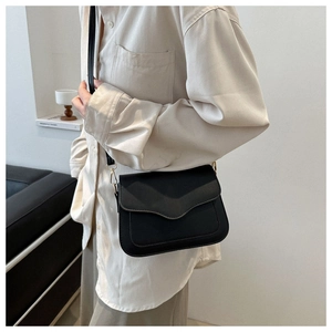 Side view of model wearing a black saddle crossbody bag with wave flap and gold hardware