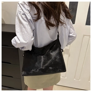 Detail of a large black leather tote bag with subtle sheen and reinforced rivets