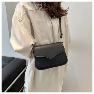 Close-up of black crossbody bag with curved flap and golden metal hardware on model