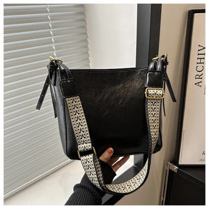 Detail of black glossy bucket bag with patterned wide strap and gold hardware