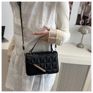 Detail of black geometric quilted handbag with gold hardware and long shoulder strap