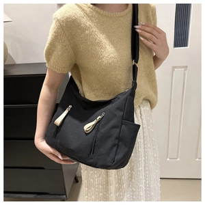 Detail of black canvas dumpling bag featuring dual zipper pockets and beige pull tabs