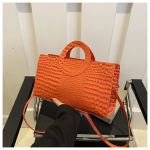 Detail of vibrant orange croc-embossed handbag with unique circular cutout handle