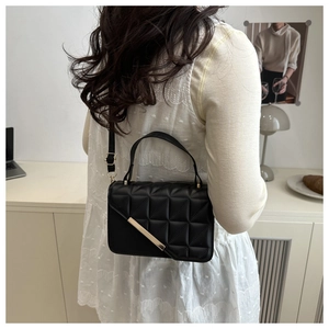 Detailed view of black quilted leather shoulder bag with gold hardware on a model