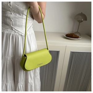 Detailed view of bright green leather baguette bag worn with a white pleated dress