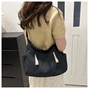 Detail of black canvas half-moon bag featuring silver zippers and white leather pulls