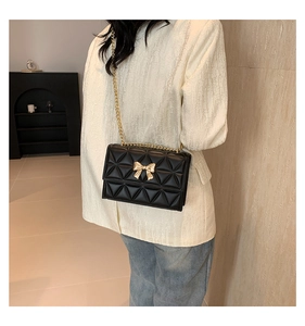 Close-up of black quilted shoulder bag featuring gold bow lock and metal chain strap
