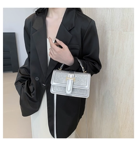 Detailed view of silver glitter crossbody bag with gold H-buckle worn on a black blazer