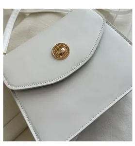 Détail d'un sac bandoulière en cuir blanc avec boucle ronde en métal doré texturé