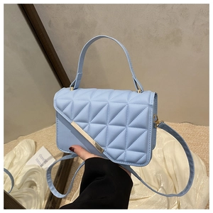 Close-up of light blue quilted handbag featuring a distinct gold metal bar on the front