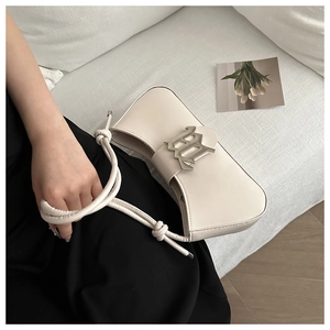 Detail of a creamy white underarm bag with a silver B-buckle and twisted rope handle