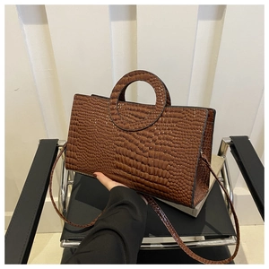 Detail of dark brown croc-embossed texture and round hollow handle on a tote bag