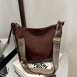 Retro burgundy leather bucket bag with a wide geometric woven shoulder strap in high gloss