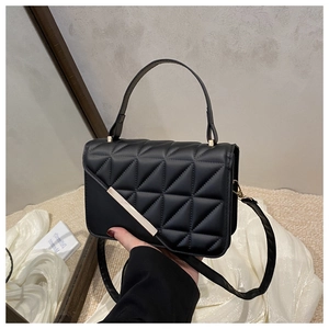 Detail of black quilted shoulder bag featuring triangular stitching and gold metal trim