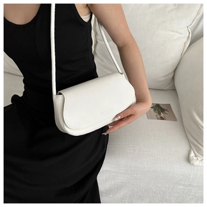Detail of white PU leather shoulder bag with Fashion logo on flap worn by model