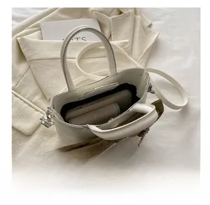 Détail d'un sac à main blanc avec nœud en velours vert et chaîne argentée montrant la capacité