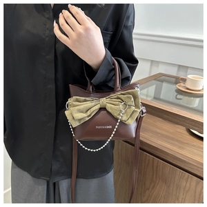 Detailed close-up of brown bucket bag featuring a large green bow and silver chain