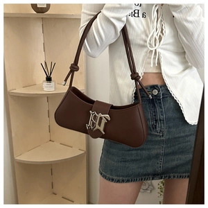 Close-up of brown leather shoulder bag featuring a silver gothic letter logo and knot detail