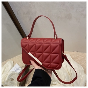 Close-up of a burgundy quilted handbag with triangular stitching and gold metal bar