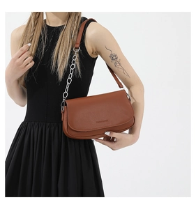 Close-up of caramel leather saddle bag with silver chain strap and embossed text