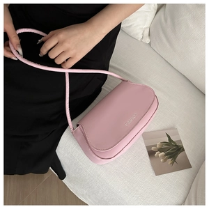 Detail of pink faux leather crossbody bag with Fashion logo on a white sofa setting
