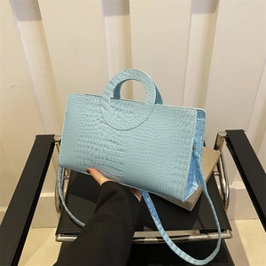 Light blue crocodile pattern tote bag with circular handle on a modern chair