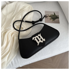 Detail of a black leather underarm bag featuring a silver metal M buckle and knotted strap