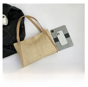 Top view of beige straw tote bag with brown leather straps next to modern electronics