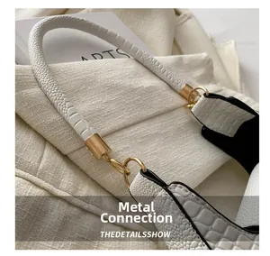 Detailed view of the gold metal connector on a white crocodile pattern shoulder bag
