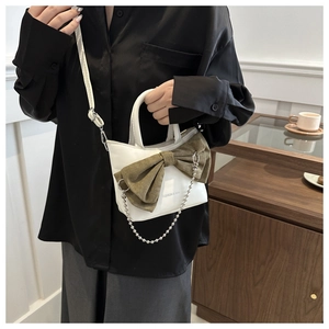 Close-up of a white leather bucket bag featuring a green corduroy bow and silver chain