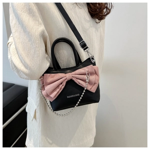 Detail of crossbody bag with black matte body and a large pink pleated bow accent