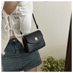 Détail du sac à rabat en cuir noir avec boucle dorée porté sur une tenue en denim