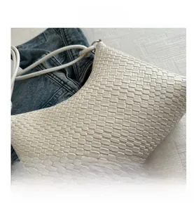 Close-up of white woven leather texture on a stylish crossbody bag over blue denim